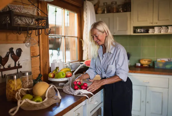 Glad äldre kvinna packa upp shopping inomhus hemma, hållbar livsstil. — Stockfoto