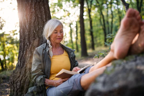 Seniorin entspannt sich und liest Buch im Wald. — Stockfoto