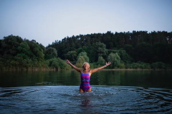 Mutlu aktif yaşlı kadın yüzücü göle su sıçratıyor.. — Stok fotoğraf
