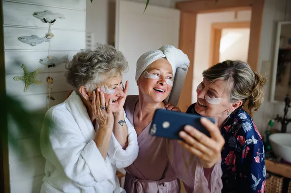 Boldog idősebb nők barátok fürdőköpenyben szelfit otthon, önellátás koncepció. — Stock Fotó