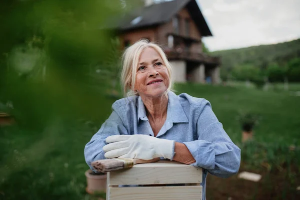 Happy senior kobieta siedzi i odpoczywa podczas malowania rzemiosła na zewnątrz w ogrodzie. — Zdjęcie stockowe