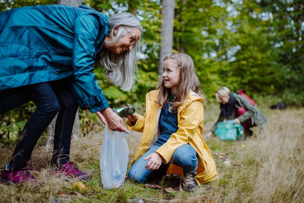 Small girl with mother and grandmother picking up waste outoors in forest. — Stock Photo, Image
