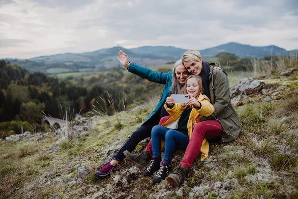 Liten flicka med mor och mormor tar selfie utflykter på toppen av berget. — Stockfoto