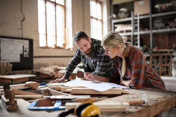 Dos carpinteros hombre y mujer mirando planos en interiores en taller de carpintería. — Foto de Stock