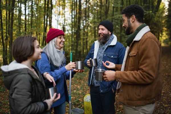 Rozmanitá skupina šťastných dobrovolníků uklízí les, dává si pauzu, pije čaj a mluví spolu. — Stock fotografie