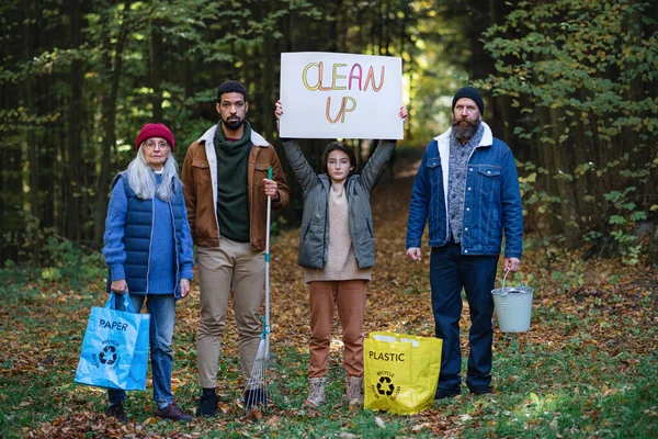 Разнообразная группа раздраженных активистов, готовых очистить лес, держать баннер и смотреть в камеру. — стоковое фото