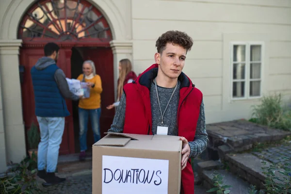 Gruppe junger Ehrenamtlicher übergibt Spendenbox an Seniorin, die vor der Tür steht, Sozialkonzept — Stockfoto