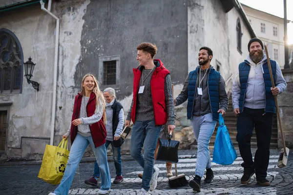 Vielfältige Gruppe von glücklichen Freiwilligen, die mit Werkzeugen für Straßenreinigung, Gemeinschaftsdienstkonzept, unterwegs sind — Stockfoto