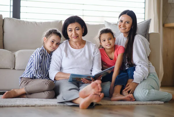 Gelukkig kleine meisjes met moeder en oma binnen thuis, zitten op de vloer en kijken naar de camera — Stockfoto