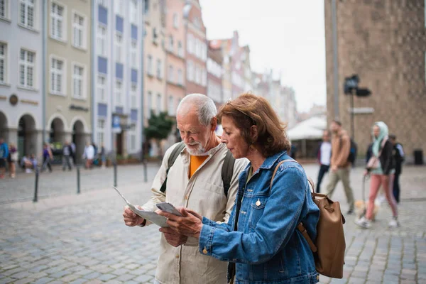 Retrato de pareja de turistas mayores utilizando el mapa y el teléfono inteligente al aire libre en la calle de la ciudad —  Fotos de Stock