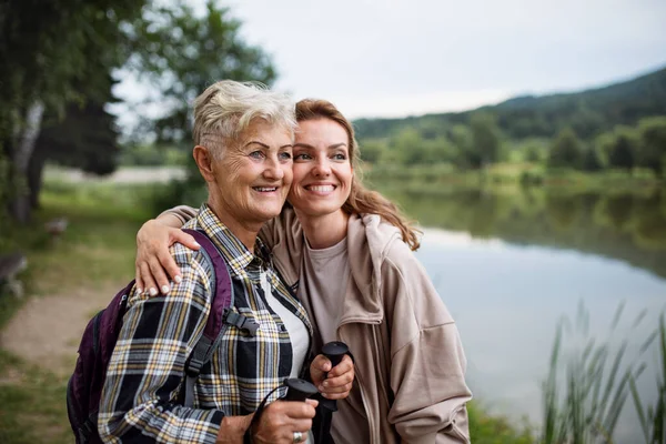 Счастливая старшая мать турист объятия со взрослой дочерью на озере на природе — стоковое фото