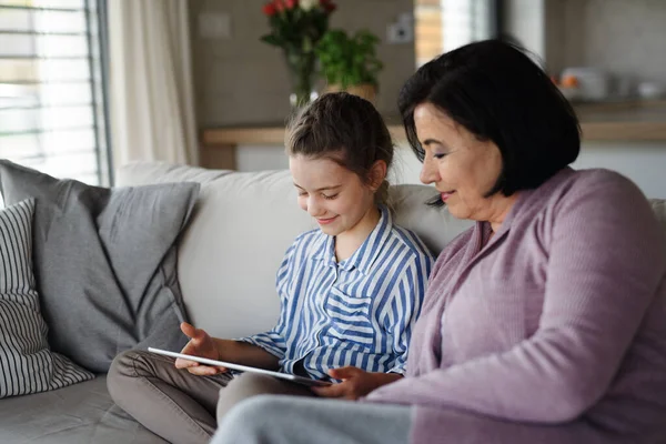 Feliz niña pequeña con la abuela en el interior de casa, utilizando la tableta. — Foto de Stock