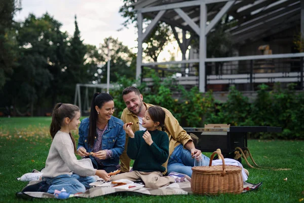 Feliz familia joven sentada en una manta y teniendo un picnic para llevar al aire libre en el área del restaurante. — Foto de Stock