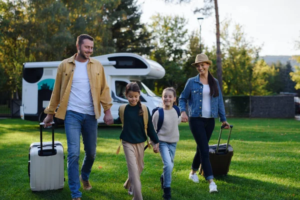 Felice giovane famiglia che cammina con valigie, tornando a casa dal viaggio in roulotte all'aperto in giardino — Foto Stock