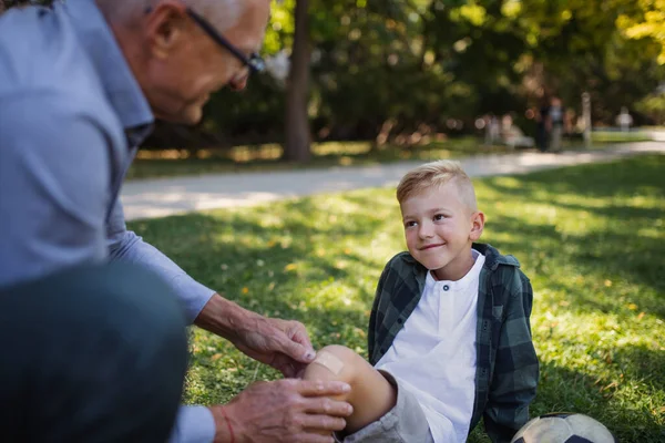 Kleiner Junge mit verletztem Bein bekommt Gips vom Großvater im Park. — Stockfoto