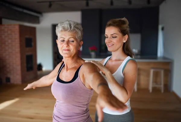 Активная пожилая женщина в спортивной форме упражняется с женской физиотерапевт в помещении дома. — стоковое фото