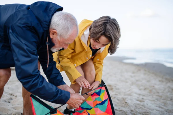 Älterer Mann und seine Enkelin bereiten Drachen für das Fliegen am Sandstrand vor. — Stockfoto