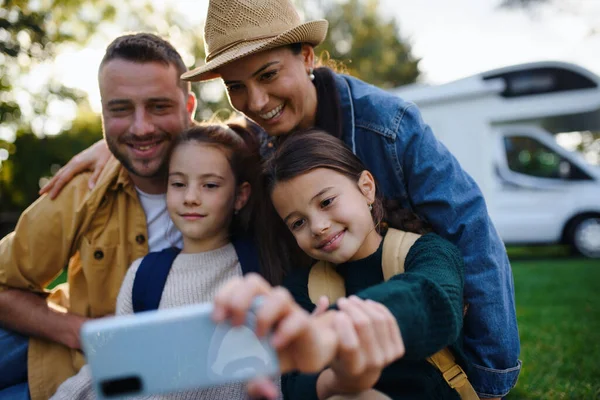 Šťastná mladá rodina se dvěma dětmi ltaking selfie s karavanou v pozadí venku. — Stock fotografie