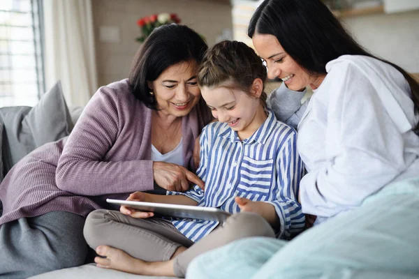 Gelukkig klein meisje met moeder en grootmoeder binnen thuis, met behulp van tablet. — Stockfoto