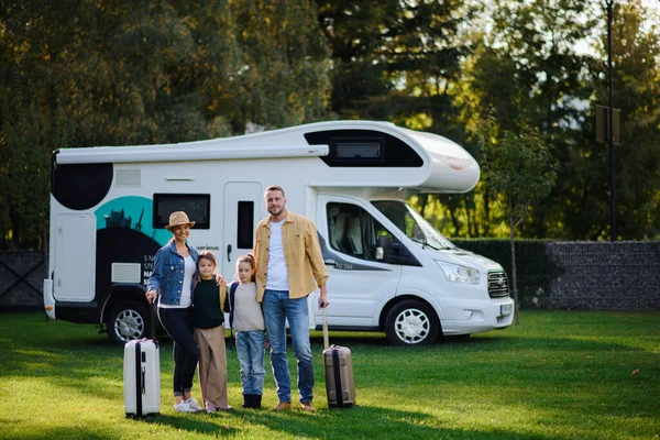 Feliz jovem família com bagagem olhando para a câmera com campista no fundo ao ar livre no jardim. — Fotografia de Stock