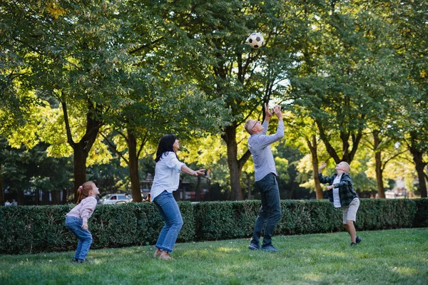 Щасливі маленькі діти з дідусем і бабусею грають з футболом на відкритому повітрі в парку — стокове фото