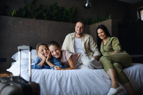 Boldog fiatal család két gyerekkel az ágyon fekve és a kamerába nézve a szállodában, nyári szünetben. — Stock Fotó
