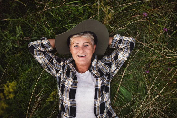 Draufsicht auf glückliche Bäuerin, die auf Gras liegt und draußen auf der Wiese in die Kamera schaut. — Stockfoto