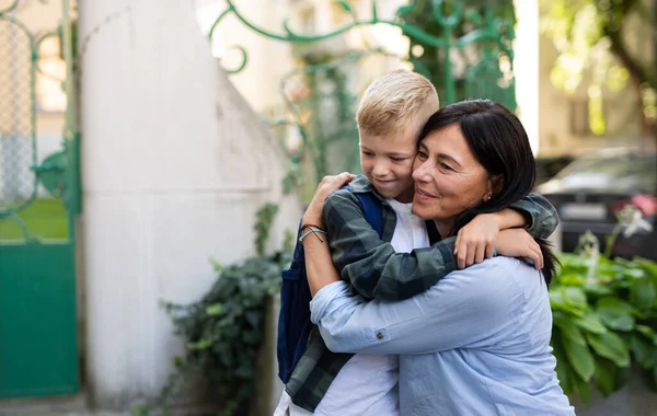 Feliz colegial abrazando a su abuela esperándolo después de la escuela al aire libre en la calle. — Foto de Stock