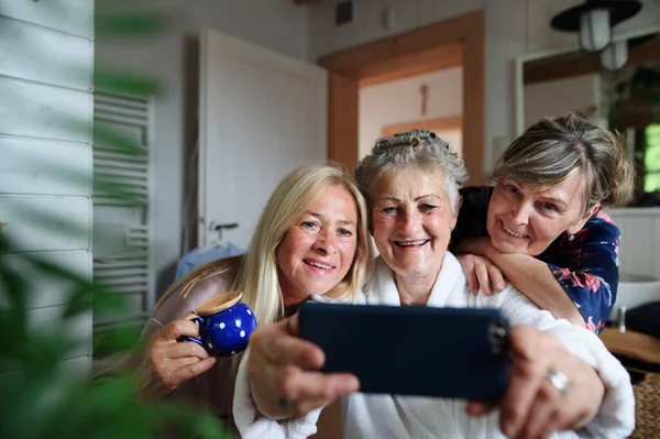 Szczęśliwy starszy kobiety przyjaciele w szlafroki biorąc selfie w domu, samoopieki koncepcja. — Zdjęcie stockowe