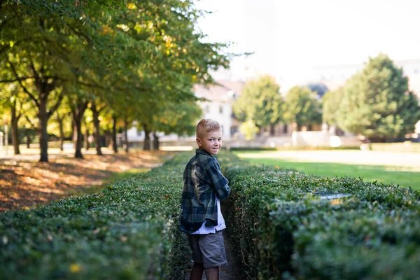 Щасливий маленький хлопчик обертається навколо і дивиться на камеру при ходьбі на вулиці в парку — стокове фото