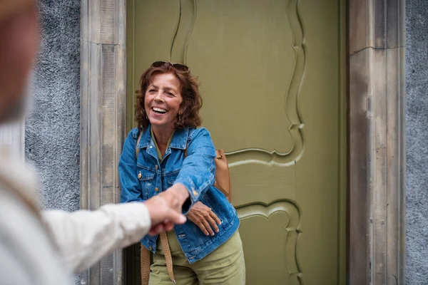 Gelukkig senior vrouw geeft hand aan senior man, paar in de liefde houden buiten in de stad — Stockfoto
