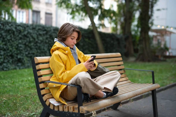 Liseli kız bankta oturuyor ve açık havada akıllı telefon kullanıyor.. — Stok fotoğraf