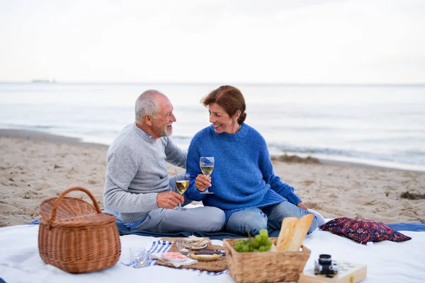Счастливая влюбленная старшая пара, сидящая на одеяле и обнимающаяся во время пикника на пляже — стоковое фото