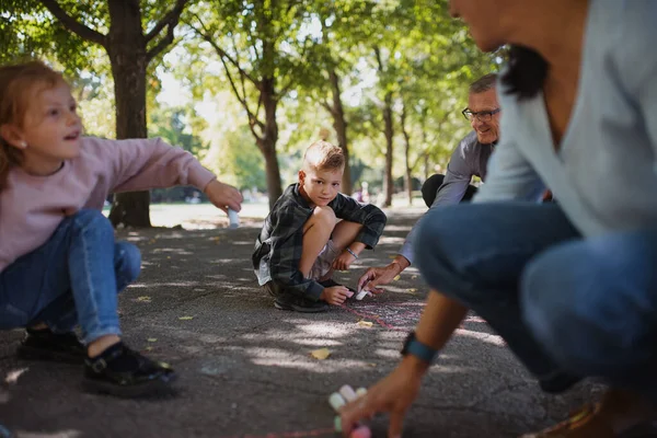 Casal sênior com netos desenho com giz no pavimento ao ar livre no parque. — Fotografia de Stock