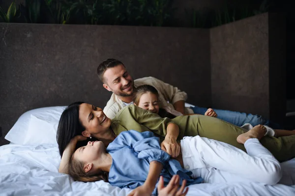 Щаслива молода сім'я з двома дітьми лежить на ліжку в готелі, літній відпочинок . — стокове фото