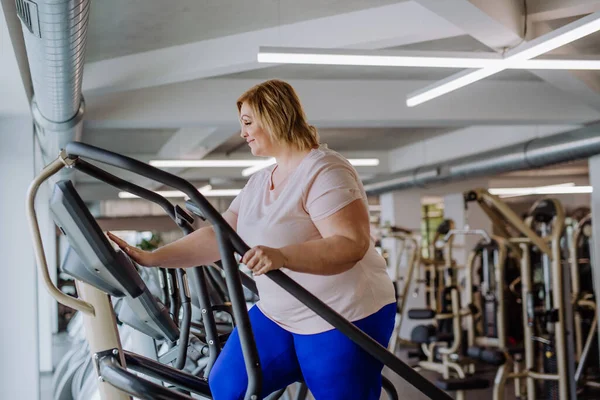 Feliz mediana mujer adulta con sobrepeso haciendo ejercicio en stepper interior en el gimnasio —  Fotos de Stock