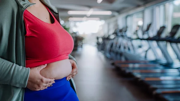 Midsection de femme en surpoids en vêtements de sport montrant son ventre excessif à l'intérieur dans la salle de gym — Photo