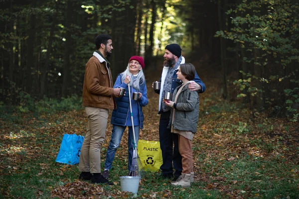Rozmanitá skupina šťastných dobrovolníků uklízí les, dává si pauzu, pije čaj a mluví spolu. — Stock fotografie