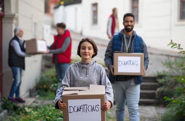 Preteen girl volunteer with team delivering donation boxes and looking at camera, social care concept — Stock Photo, Image