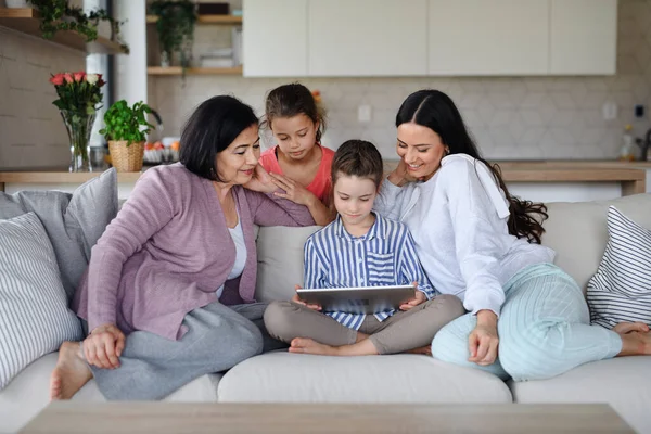 Niñas felices con la madre y la abuela en casa, sentadas en el sofá y usando la tableta. — Foto de Stock