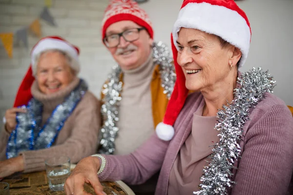 Amigos seniores felizes sentados dentro de casa no centro da comunidade e celebrando o Natal. — Fotografia de Stock