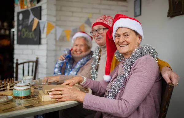 Happy senior friends sitting indoors in community center and celebrating Christmas. — Stock Photo, Image