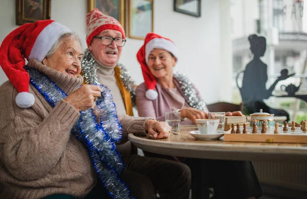 Amigos seniores felizes sentados dentro de casa no centro da comunidade e celebrando o Natal. — Fotografia de Stock