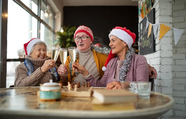 Amigos seniores felizes sentados dentro de casa em copos de champanhe de café e celebrando o Natal. — Fotografia de Stock