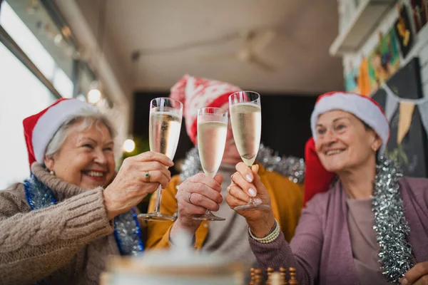Happy senior friends sitting indoors in cafe clinking champagne glasses and celebrating Christmas. — Stock Photo, Image