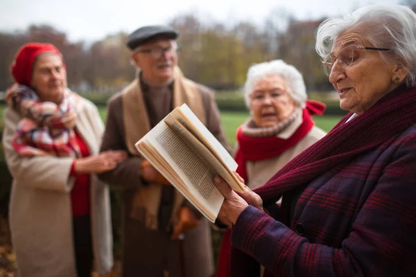 Sonbaharda parkta kitap okuyup sohbet eden bir grup mutlu kıdemli arkadaş.. — Stok fotoğraf