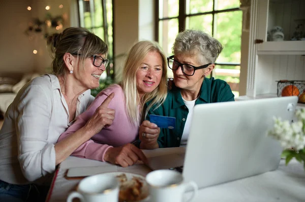 Счастливые старшие друзья, пользующиеся ноутбуком и кредитной картой дома, кофе. — стоковое фото