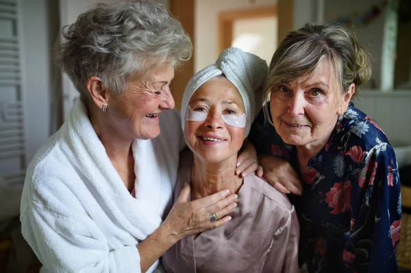 Ευτυχισμένες ηλικιωμένες φίλες με μπουρνούζια κοιτάζουν την κάμερα μέσα στο σπίτι, την ιδέα της αυτοφροντίδας. — Φωτογραφία Αρχείου