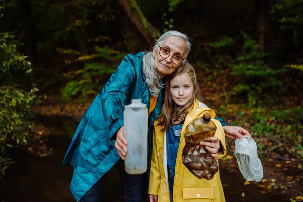 Klein meisje met oma tonen plastic afval wat ze vonden outoors in het bos. — Stockfoto
