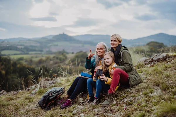 Small girl with mother and grandmother sitting and lookiong at view on top of mountain. — Stock Photo, Image